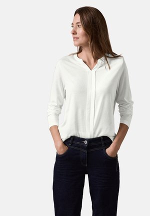 Witte blouse met lange mouwen en een V-hals, gecombineerd met donkerblauwe, lichtgetextureerde jeans met zichtbare stiksels en zakken.