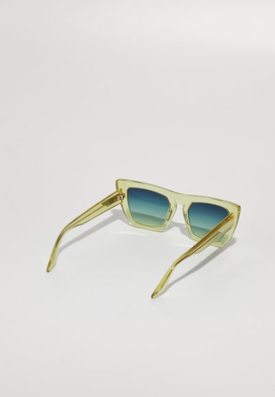 Transparente gelbe Sonnenbrille mit einem geometrischen Rahmen, ausgestattet mit einer blauen Verlaufslinse und dünnen Bügeln mit goldenen Akzenten.
