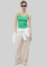 Top verde fittings, pantaloni lungi bej din in, cămașă albă din in legată la talie și ochelari de soare negri. Sandalele simple completează aspectul.