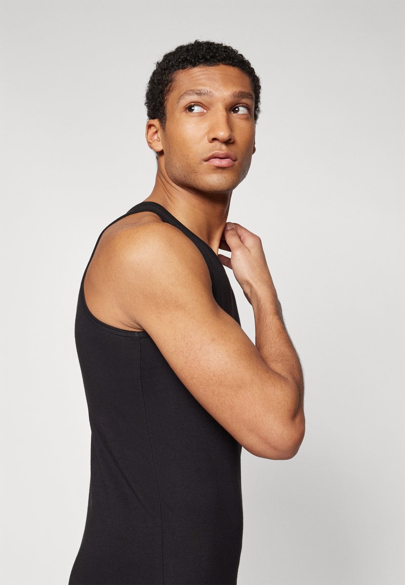 Czarny top na ramiączkach wykonany z gładkiego, lekkiego materiału. Posiada dopasowany krój, okrągły dekolt i ramiączka. Minimalistyczny design.