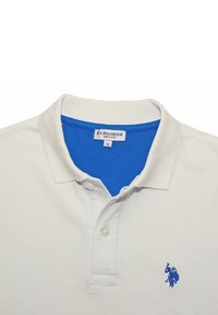 Vitt polo-shirt med blå inre krage, två knappar och blått broderat polo-spelare-logotyp på vänster bröst.