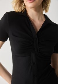 Black ribbed short-sleeve shirt with a collared neckline, gathered front detail, and black buttons down the center. Smooth texture.