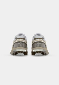 Gray and beige athletic shoes with mesh upper, padded collar, reflective accents, and textured rubber sole. Features "GEL" branding.