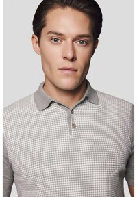 Szary polo z teksturowanym wzorem w zębatkę, krótkimi rękawami i kołnierzykiem zapinanym na guziki, wykonany z miękkiego dzianinowego materiału.