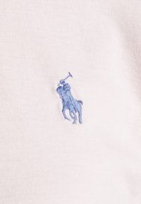Lätt bomullspiké med en liten, blå broderad polo-spelare logotyp på vänster bröst. Tyget har en slät yta.