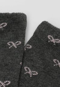 Grå stickade strumpor med ett mönster av små, ljusrosa rosetter. Texturen är mjuk, med ribbade muddar längst upp.