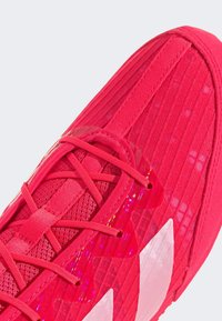 Scarpa sportiva rossa con tomaia in mesh texture, diverse designs di strap e accenti riflettenti. Presenta una forma elegante e aerodinamica.