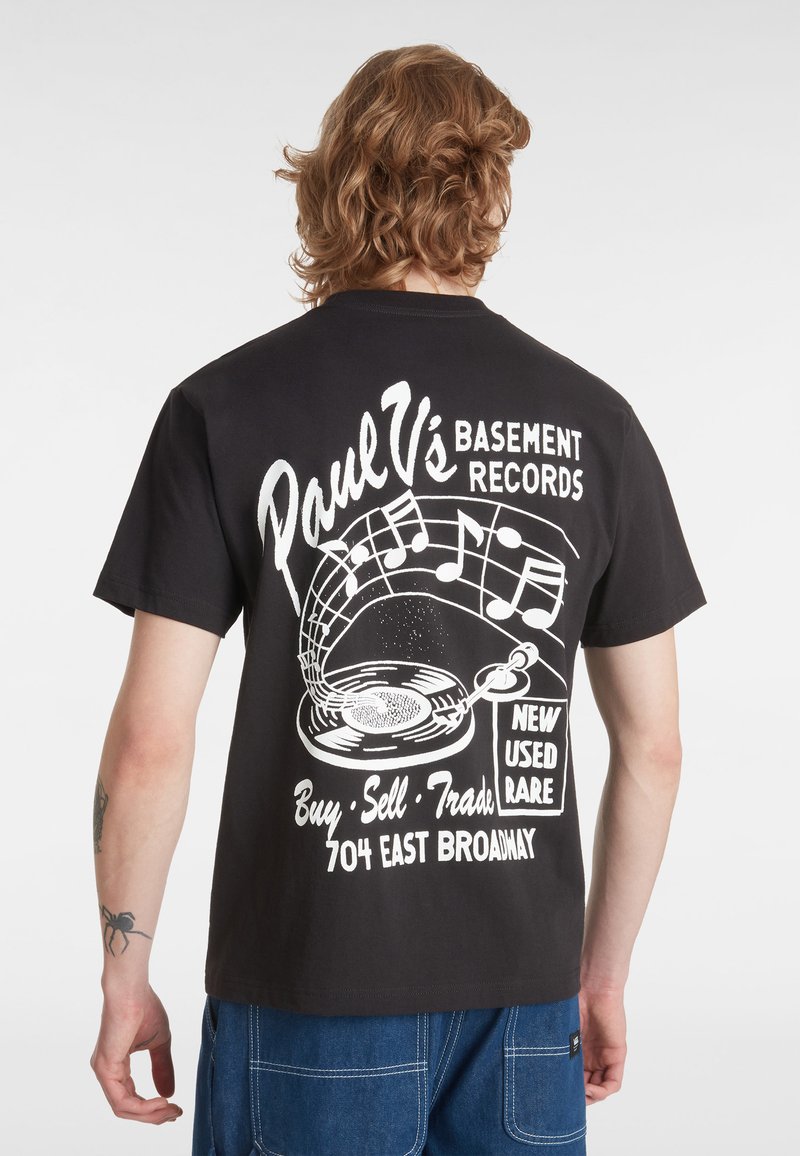 Camiseta de algodón negra con una impresión gráfica blanca de un tocadiscos y notas musicales, con texto sobre una tienda de discos en la parte de atrás.