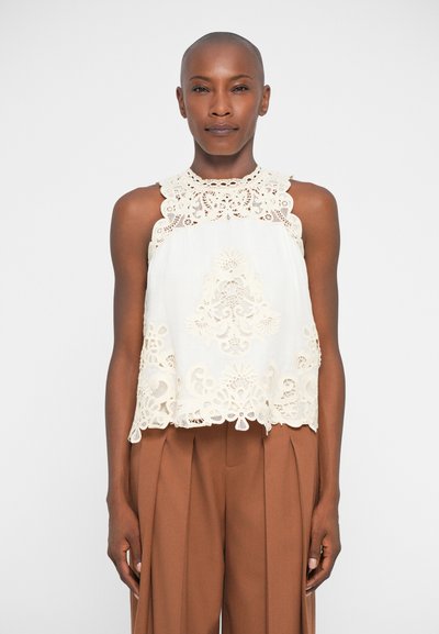 Blouse sans manches blanche avec un délicat détail en dentelle beige au niveau du col et de l'ourlet, arborant des motifs floraux et des bords festonnés.