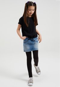 Črna majica s kratkimi rokavi z vozlom na pasu, svetlo denim krilo, črne legice in športni copati z vzorcem. Preprost in sproščen videz.