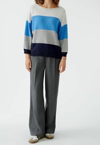 Sweter typu pulower w jasnoszare paski w odcieniach niebieskiego i granatu; posiada szeroki dekolt i ściągacze przy rękawach. Połączony z szarymi spodniami o szerokich nogawkach.