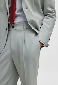Light grey suit with a textured finish, featuring a tailored fit, single button closure, and pockets. Paired with a red polka dot tie.