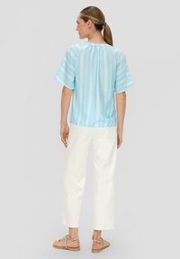 Chemise à manches courtes rayée bleu clair avec une coupe décontractée, associée à un pantalon large blanc et des sandales beiges. Texture de tissu lisse.