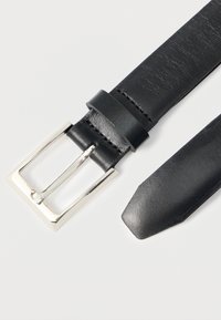 Ceinture en cuir noir avec une boucle carrée argentée, texture lisse et design à extrémité effilée. Coutures visibles le long du cuir.