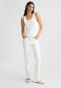 Top bianco senza maniche con scollo rotondo e dettagli con logo, abbinato a jeans bianchi a gamba larga e scarpe aperte decorate. Texture lisce.