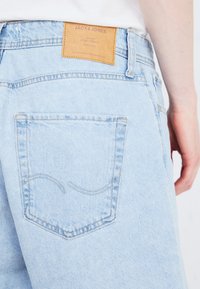Lyseblå denimjeans med et lærmerke med "JACK & JONES" på livet og en enkelt baklomme med en buet sømdetalj.
