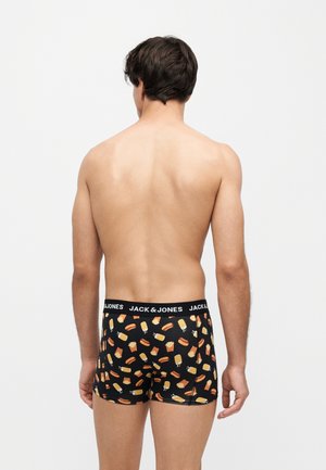 Homme debout de dos à la caméra, portant un boxer noir avec un motif fast-food et une ceinture avec le logo Jack & Jones, sur un fond uni clair.