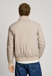 Ljusbeige puffjacka med ståkrage, ribbade ärmslut och midja. Slät textur, fylld för isolering. Avslappnad design.