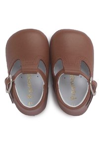 Zapatos de cuero marrón con diseño troquelado, correa ajustable y interior blanco. Presentan una textura suave y un logotipo dorado en la plantilla.