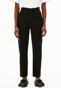 Jeans noirs taille haute à jambe droite, fabriqués en denim, avec cinq poches et une fermeture à bouton sur le devant. Associés à des mocassins noirs à franges.