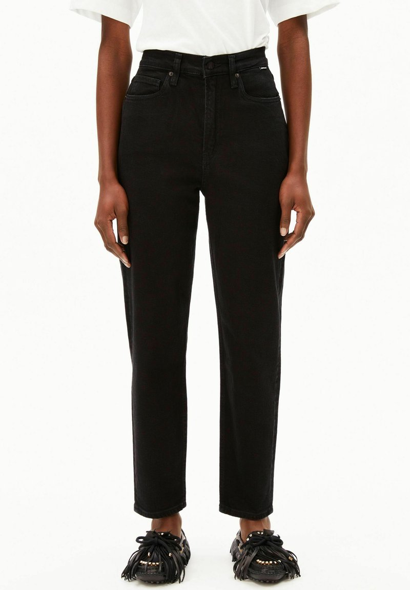 Jeans noirs taille haute à jambe droite, fabriqués en denim, avec cinq poches et une fermeture à bouton sur le devant. Associés à des mocassins noirs à franges.