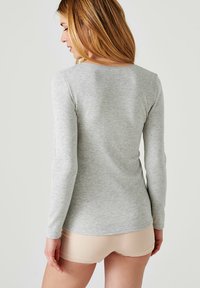 Grijze lange mouwen top met een ronde hals; zachte textuur; aansluitend ontwerp; gedragen met lichtbeige shorts, die een glad profiel van de rug laten zien.