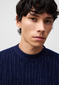 Maglione blu navy con sottili motivi a strisce verticali, girocollo classico, trama morbida e design aderente.