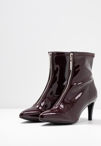 Bottines en cuir verni bordeaux à bout pointu, fermetures éclair latérales et talon de 3 pouces ; texture lisse avec coutures décoratives.