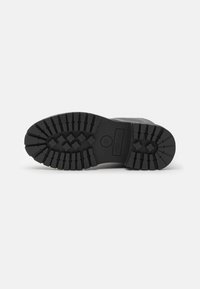 Black rubber boot sole with deep treads and an angular shape. Features a small circular logo and distinct hexagonal pattern for traction.