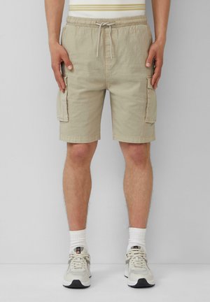 Shorts cargo beiges avec une taille élastique et un cordon de serrage, dotés de poches latérales et d'un tissu texturé. Portés avec des baskets de couleur claire.