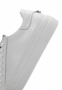 White leather sneaker with a smooth texture, displaying a low profile design, round toe, and a thick white rubber sole. Laces are white.