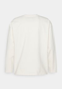 T-shirt à manches longues de couleur crème en coton. Il présente un col rond et une coupe décontractée avec des détails de couture minimaux.