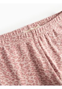 Nærbilde av rosa leopardmønstret stoff, med elastisk midje, som viser en myk tekstur og uformell design.