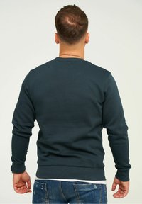 Dark teal sweatshirt with long sleeves, ribbed cuffs, and a round neckline. Smooth texture, solid color, minimalistic design, no visible patterns.