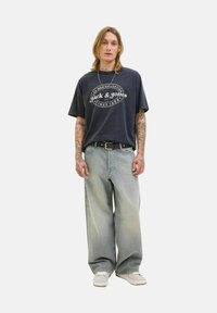 Marineblauwe katoenen t-shirt met wit gedrukt logo en een relaxte pasvorm, gecombineerd met lichtgewassen, losse denim jeans en witte sneakers.