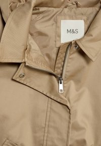 Světlá hnědá lehká bunda se zipem, patentkami a měkkou saténovou podšívkou. Obsahuje štítek "M&S" poblíž límce.