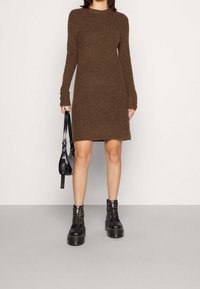 Robe longue à manches longues en tricot marron avec une coupe droite, associée à des bottes noires à lacets épaisses et un petit sac à main noir.