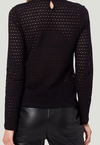 Sort langærmet top med en tekstureret, perforeret design og en nøglehulslukning bagpå. Matchet med sorte læderbukser.