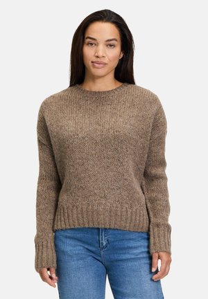 Bruine gebreide trui met een ronde hals, geribbelde mouwen en zoom, en een gestructureerde afwerking. Gecombineerd met blauwe jeans voor contrast.