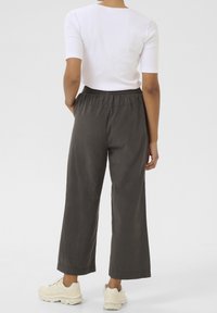 Pantalons coupe large en tissu gris foncé avec une taille élastique, associés à un haut blanc à manches courtes et des baskets de couleur claire.