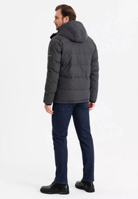 Mørkegrå dunjakke med hætte, prydet med quiltet design, forlommer og let struktureret stof, parret med mørkeblå jeans og sorte støvler.