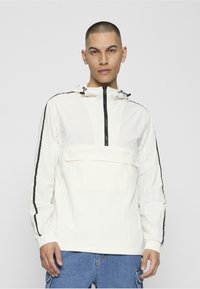 Balta viegla kapuce ar melnām sānu svītrām, priekšpuses rāvējslēdzēju un kabatu. Aprīkota ar elastīgiem aprocēm un fakturētu audumu.