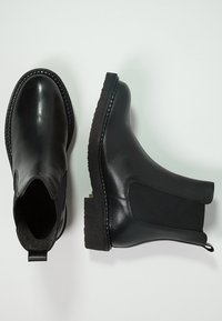 Botas Chelsea negras de cuero liso con paneles laterales elásticos, suelas de goma texturizadas y una lengüeta en la parte posterior.
