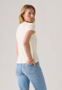 T-shirt jaune clair à manches courtes, design ajusté, tissu doux, associé à un jean taille haute bleu clair avec des détails de poche arrière.