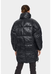 Melna pūkaina jaka ar augstu apkakli, izšūta raksta, spīdīga materiāla un elastīgām aprocēm. Rāda šauru piegriezumu un regulējamu apakšu.