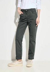 Pantalones de algodón ligeros de un verde oscuro con un corte recto, bolsillos delanteros y detalles de costura; combinados con zapatillas de deporte beiges.