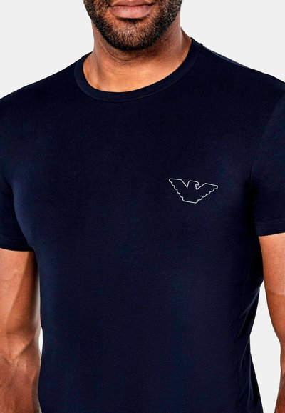 Tyrkysové bavlněné tričko s kulatým výstřihem a krátkým rukávem. Na levé straně hrudníku je bílé logo orla. Hladká textura.