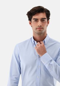 Hellblau kariertes Hemd mit Button-Down-Kragen, langen Ärmeln und weißen Knöpfen. Weicher Stoff mit glatter Textur.
