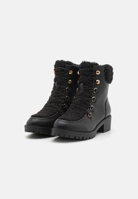 Bottes noires à lacets avec un dessus en fausse fourrure, œillets dorés et semelle texturée. Talon épais avec une finition en cuir lisse.