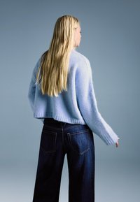 Svijetloplavi skraćeni džemper od mekane, pahuljaste tkanine, uparен s tamnoplavo širokim trapericama ravnih nogavica s džepovima na stražnjoj strani.